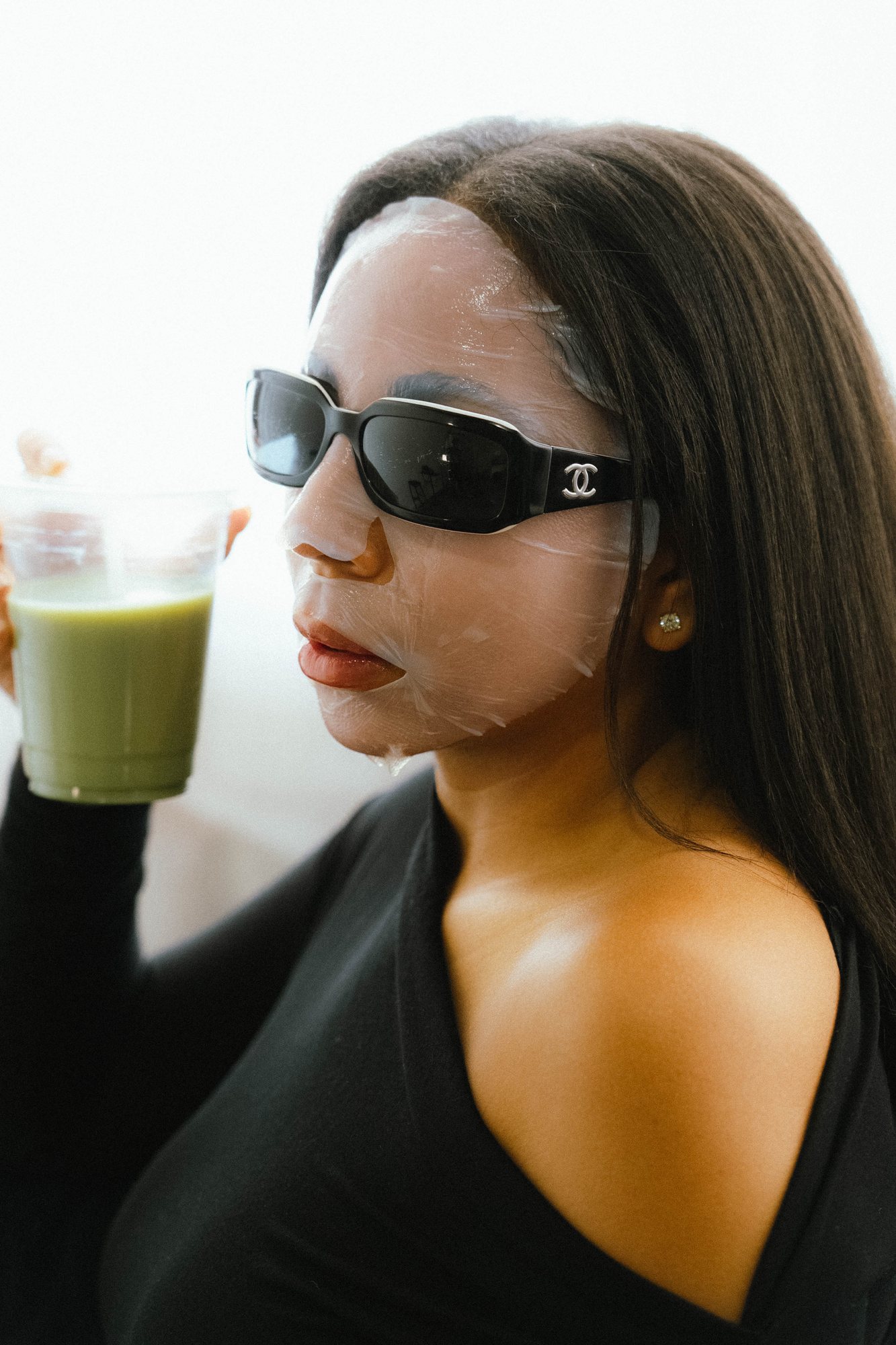 Tacha in sunglasses and a sheet mask, holding a green juice